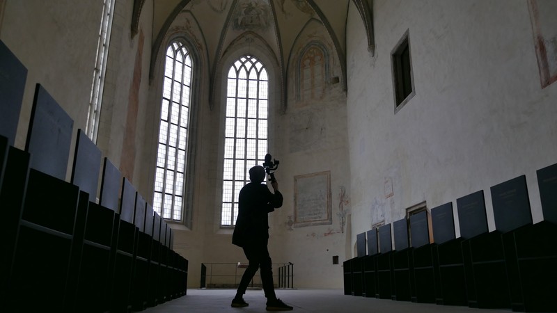 Eine Person mit Kamera filmt in der Dalheimer Klosterkirche. Rechts und links stehen schwarze Stuhlreihen.