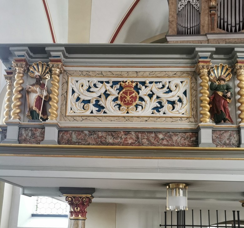 Blick in eine Kirche. Über dem Ausgang befindet sich eine Brüstung mit Schnitzereien.