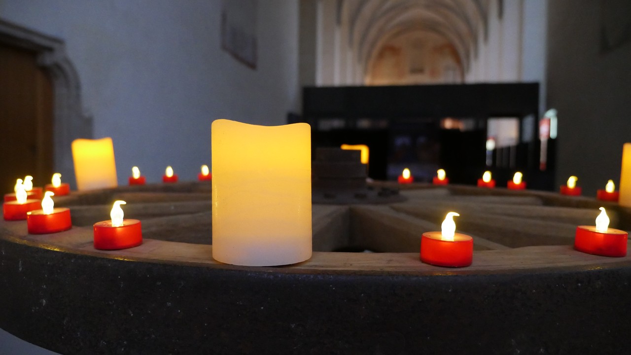 In einem dunklen Kirchenraum steht ein Wagenrad mit Kerzen.