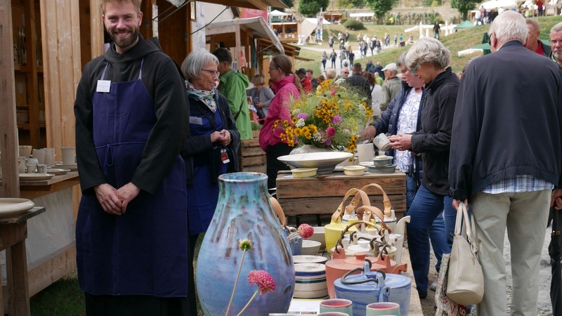 Buntes Marktgeschehen auf dem Klostergelände. Ein Ordensmann schaut lächelnd in die Kamera.