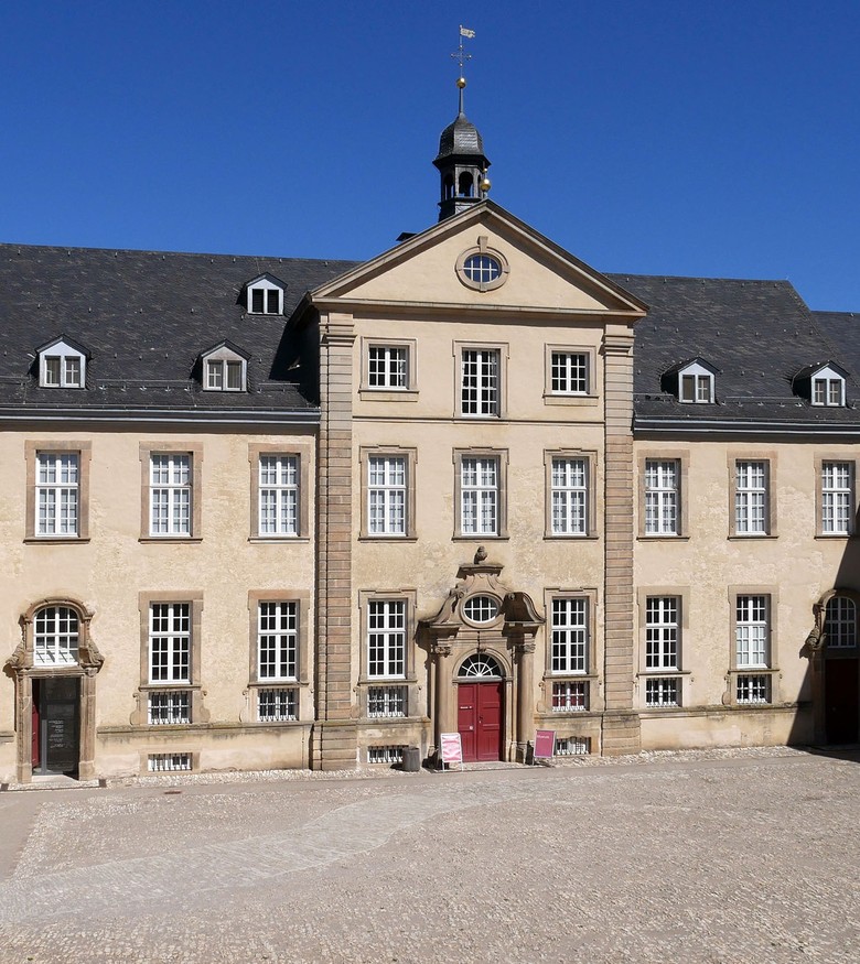 Die Fassade des Museums im Kloster Dalheim, vom Ehrenhof aus fotografiert. Die Eingangstür in der Mitte ist rot.