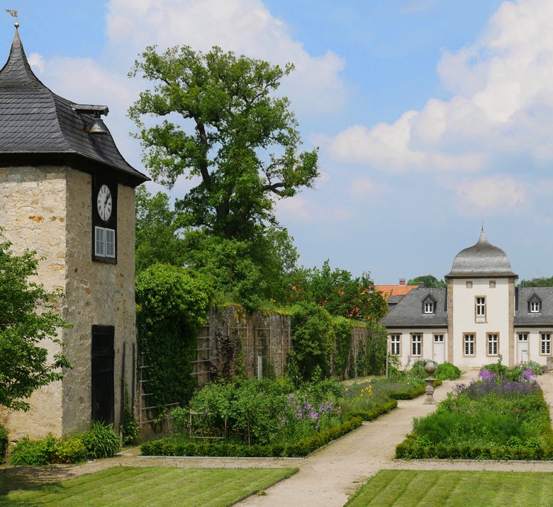 Ein Garten mit einem Uhrenturm wird von einer hohen Mauer umschlossen.